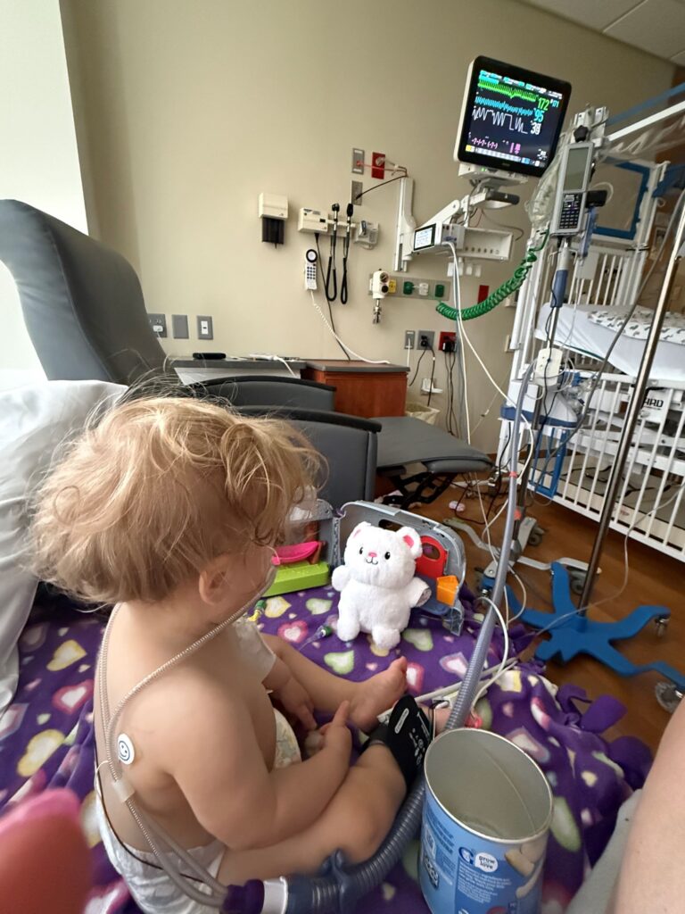 Adeline sitting in a hospital bed surrounded by medical equipment during her stay in Toledo.